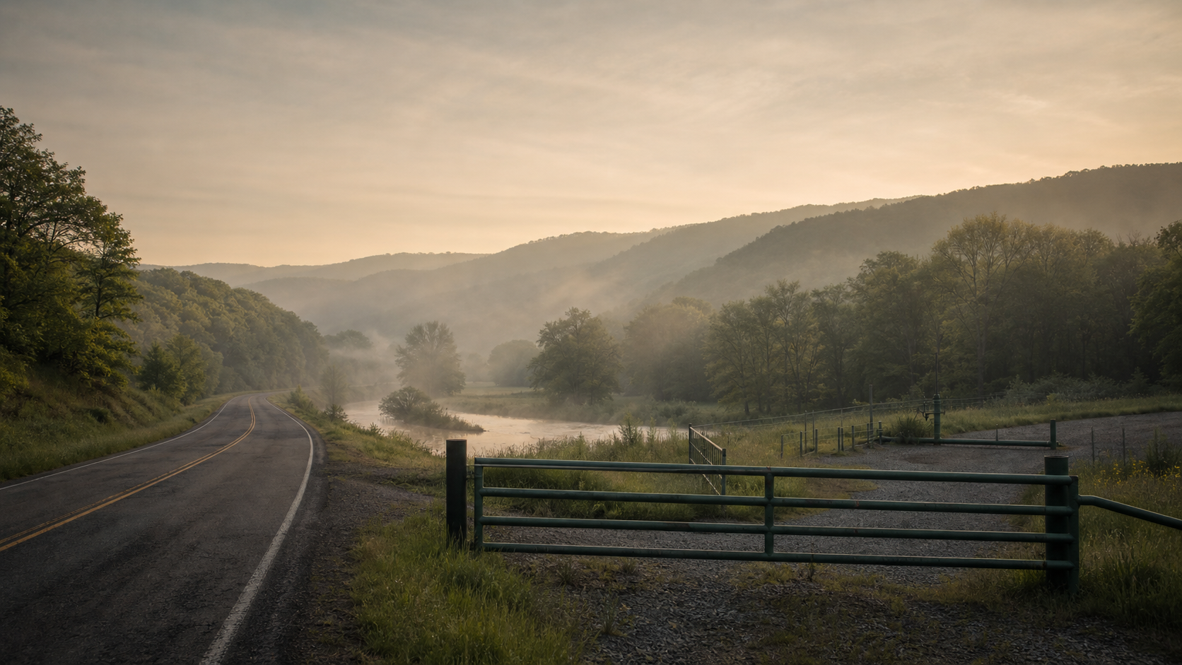 Misty late-spring dawn along a creek-side two-lane on the Pennsylvania–West Virginia border, layered Appalachian ridges in haze, a closed green pipe-gate at the entrance to a natural-gas pad.