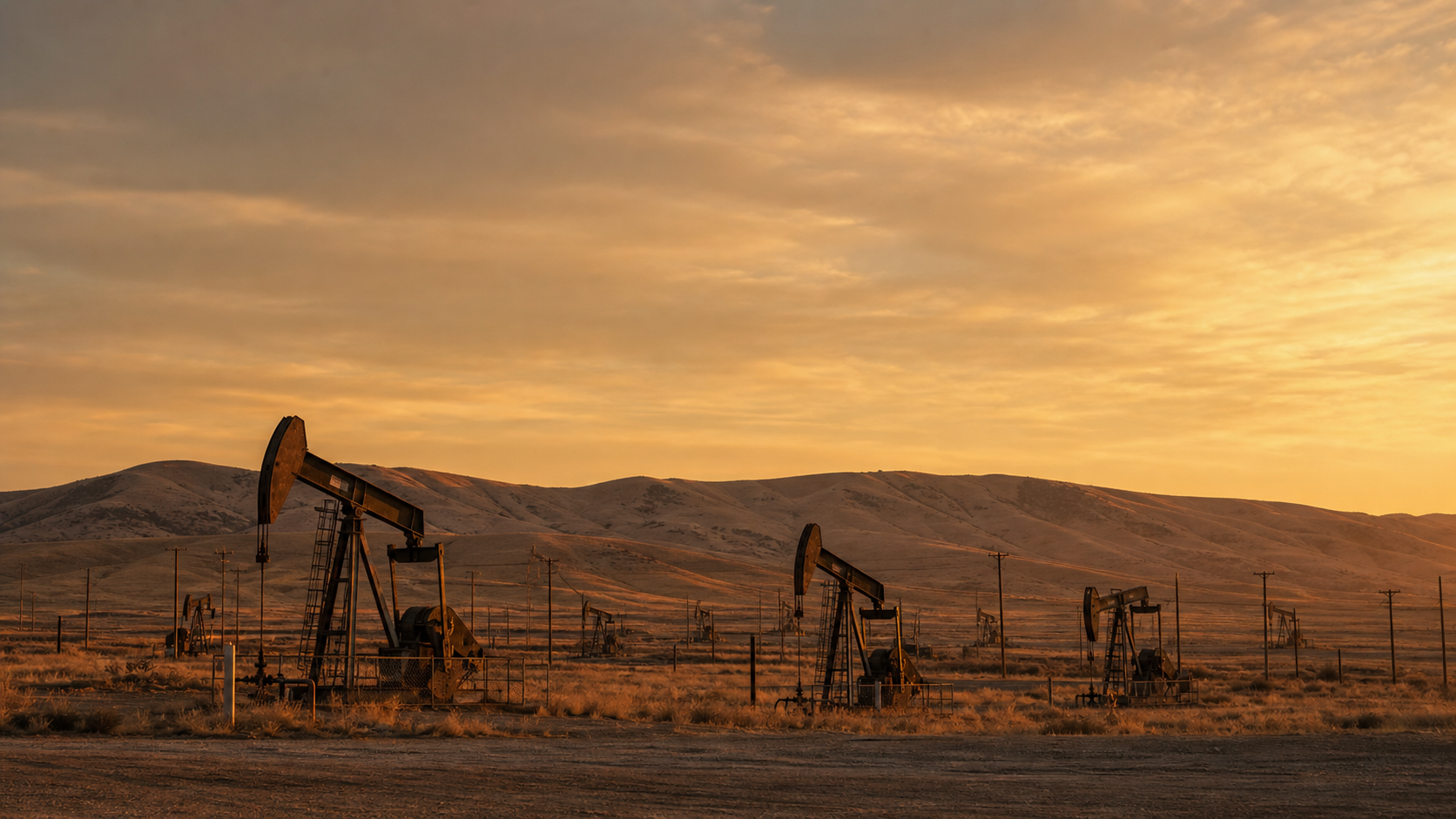 Field of vintage beam-pump units at dusk in California's San Joaquin Valley, Temblor foothills in the distance.